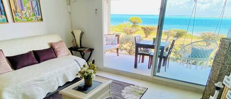 A bedroom with a large bed, a bedside table with a vase, and a view of the ocean through a sliding glass door.