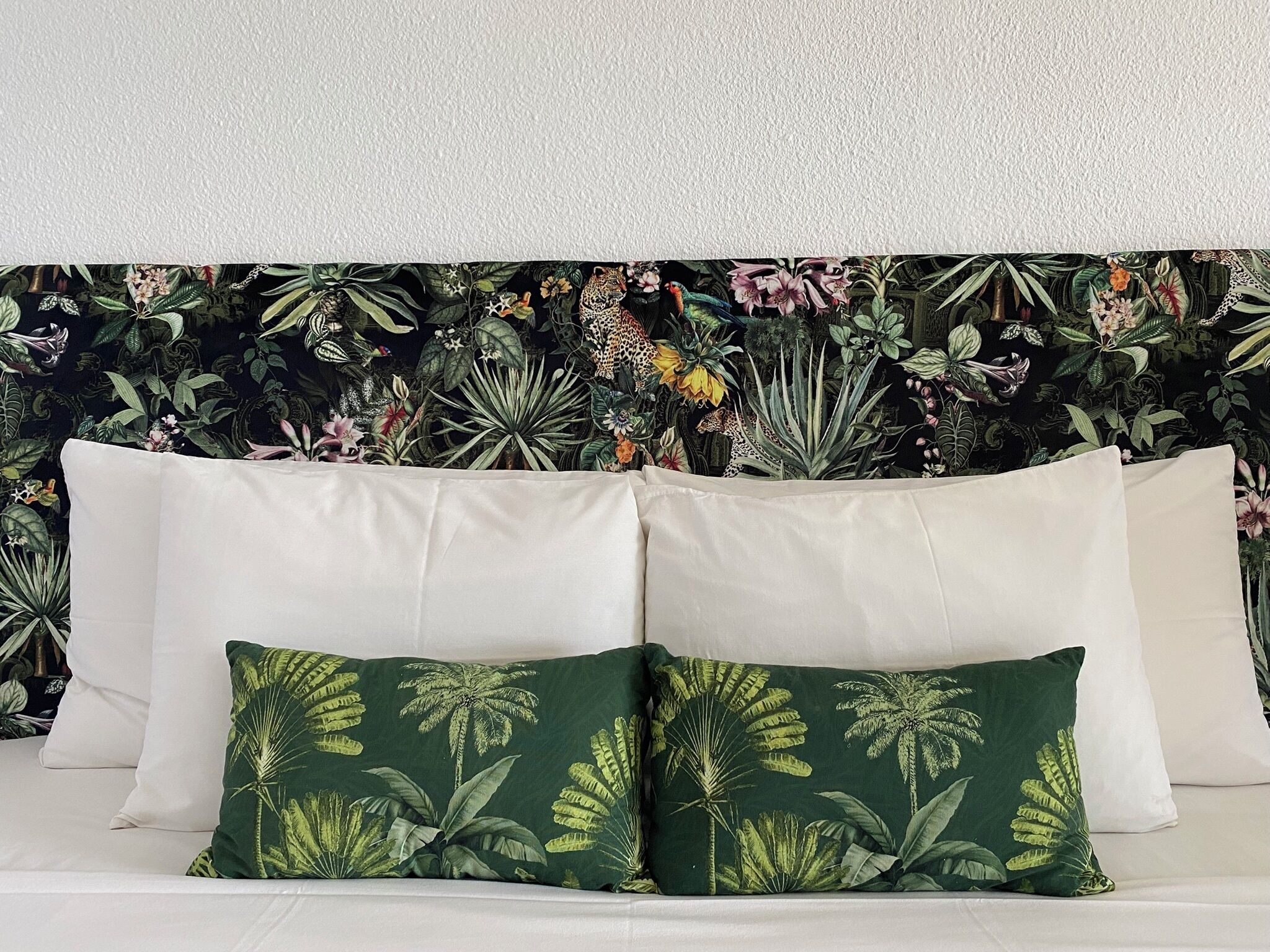 A bed with white pillows and a green pillow with a tropical leaf pattern.