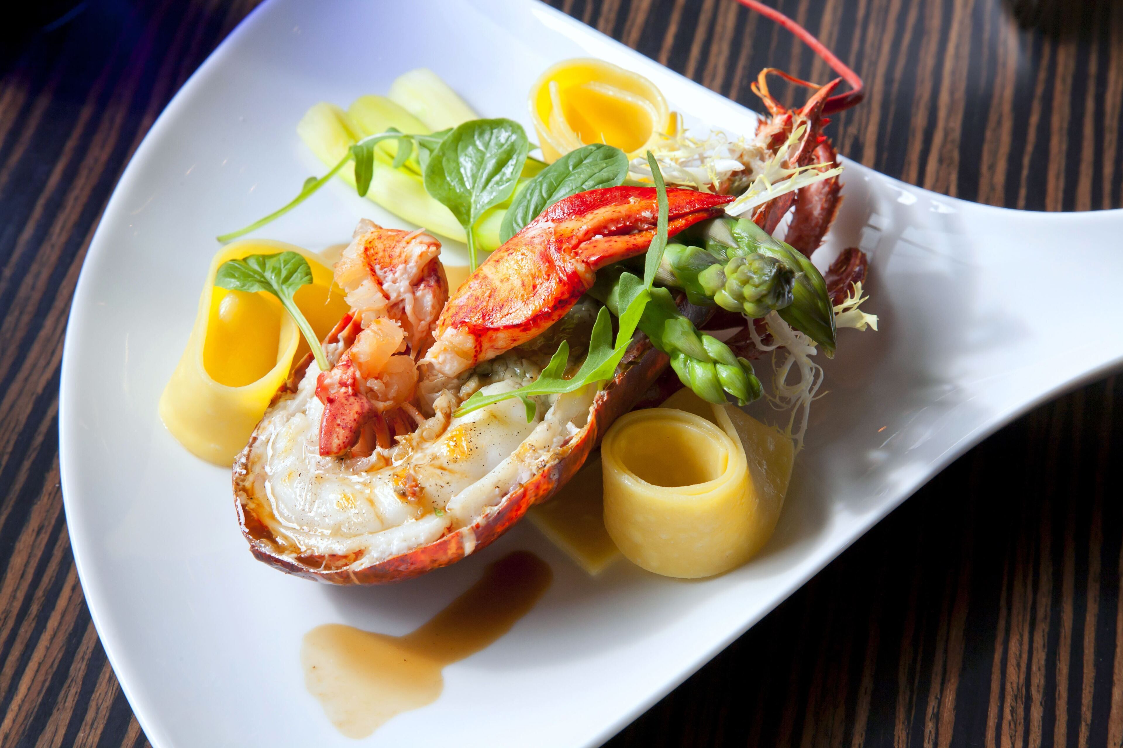 A plate of food with a lobster tail, greens, and a lemon wedge.