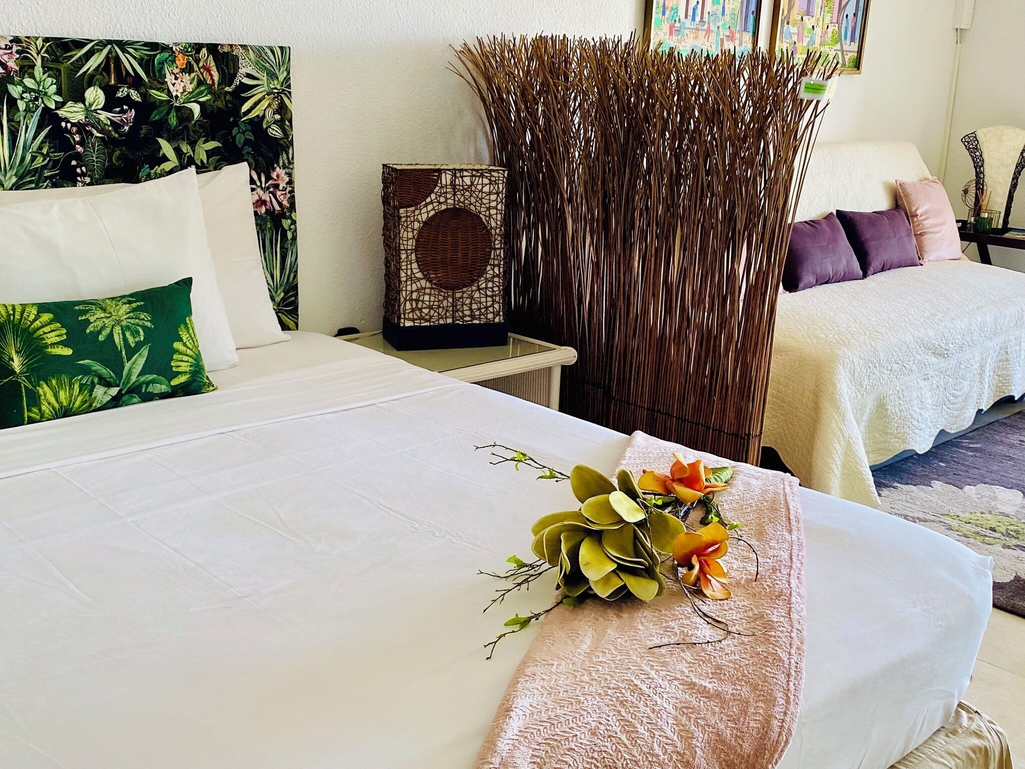 Habitación de hotel con una cama, una mesita de noche, una planta decorativa y un separador tejido.