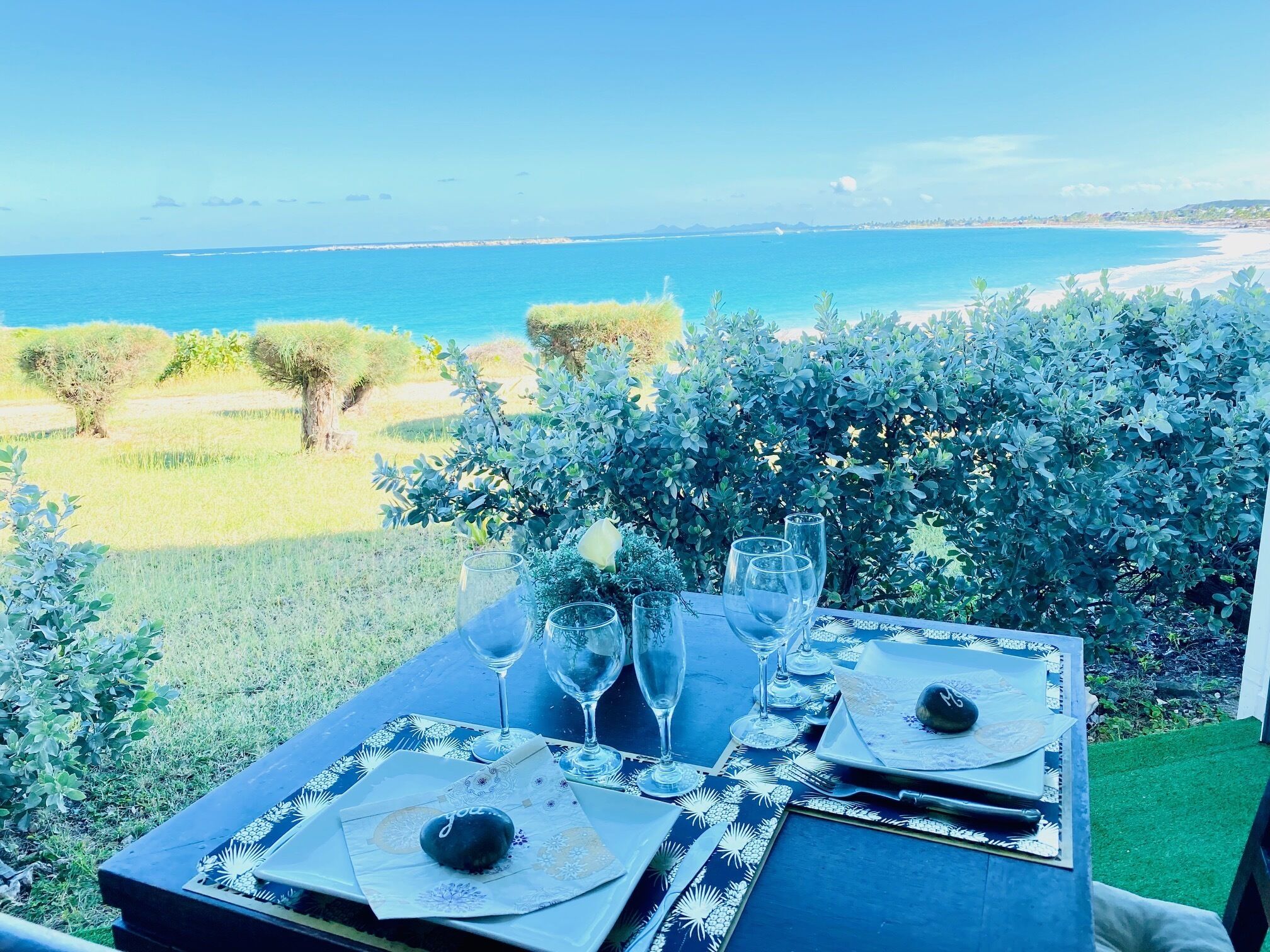 A table set for four with a view of the sea and greenery.