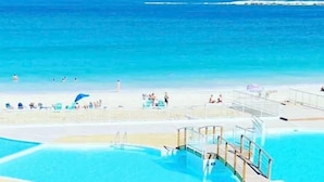 Zwembadgedeelte met helderblauw water, een redderpost en een strand op de achtergrond.