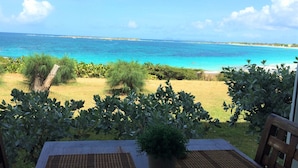 Uitzicht vanaf een balkon op een strand met helderblauw water en een gazon met struiken.
