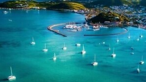 Een kustplaatsje met helder turquoise water, tal van zeilboten en een klein schiereiland met gebouwen.