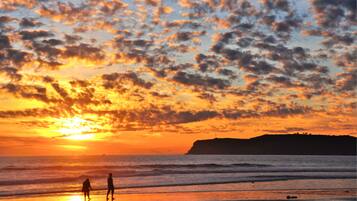 A sunset over a beach with silhouettes of people walking.