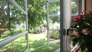 A view through a window with a mesh screen, revealing a garden with a bicycle and a house in the background. - Charming Guesthouse Studio To  Elegant 1920s Spanish Home (Coronado)