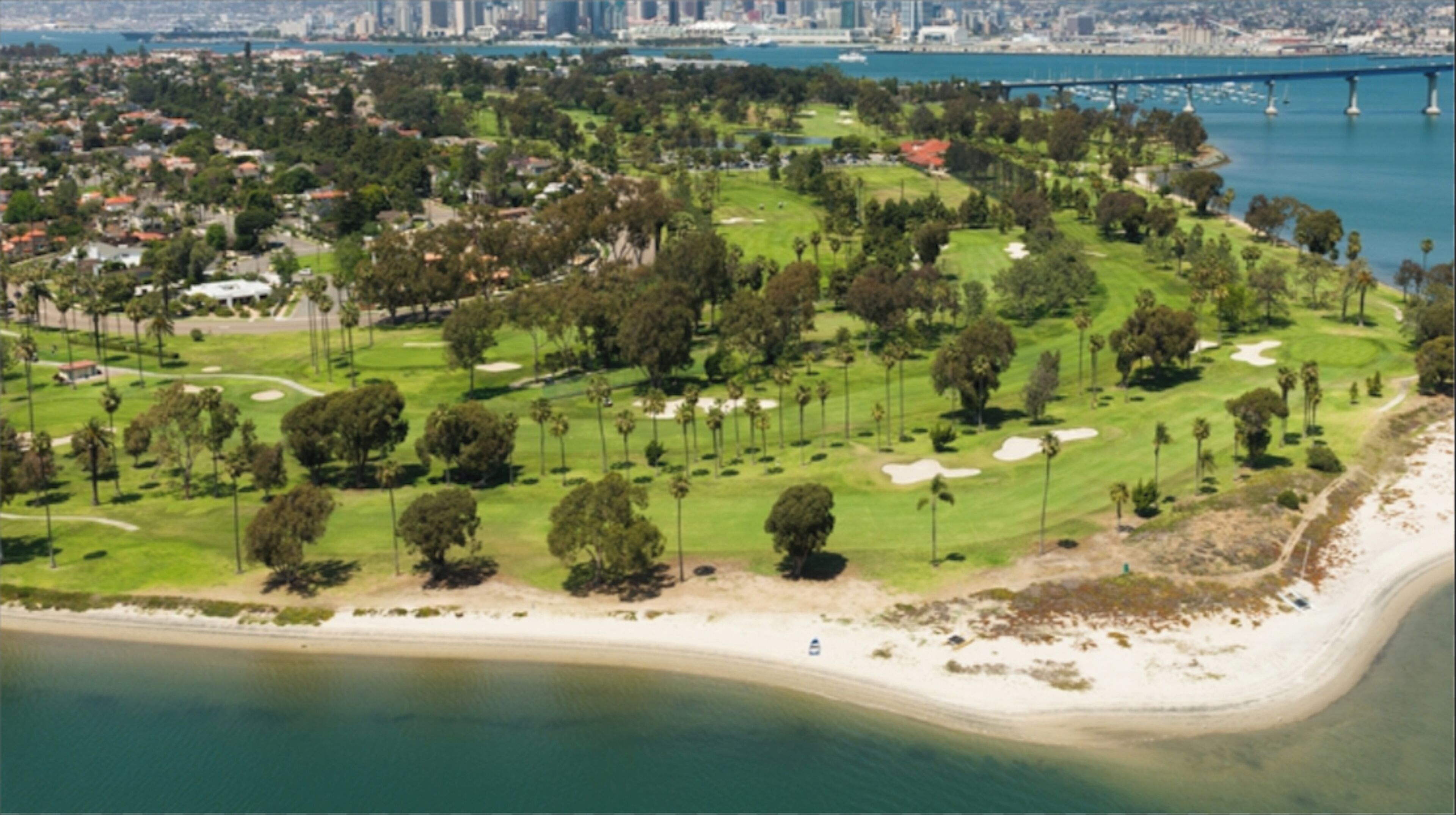 An aerial view of a coastal golf course with a bridge in the background.