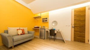 A compact living space with a sofa, a small desk, a refrigerator, and a wooden door. - Pickup Light (Tainan)
