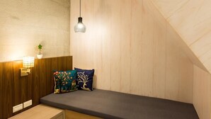 A small, cozy room with a sloped ceiling, a bench with cushions, a wall-mounted lamp, and a small plant. - Pickup Light (Tainan)