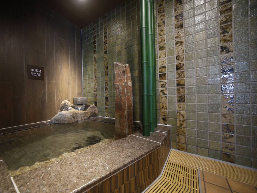 A hot spring bath area with a stone wall, a tiled wall with a grid pattern, and a wooden floor.