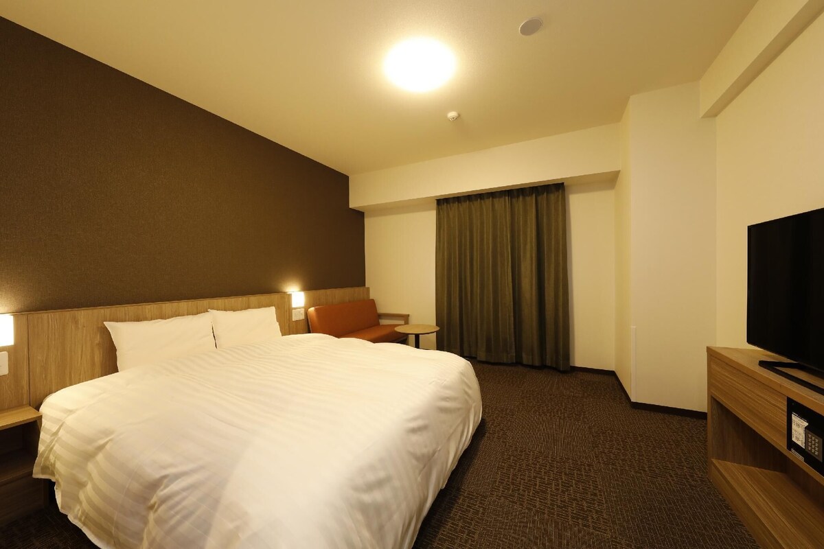 A hotel room with a large bed, a TV, a desk, and a chair.