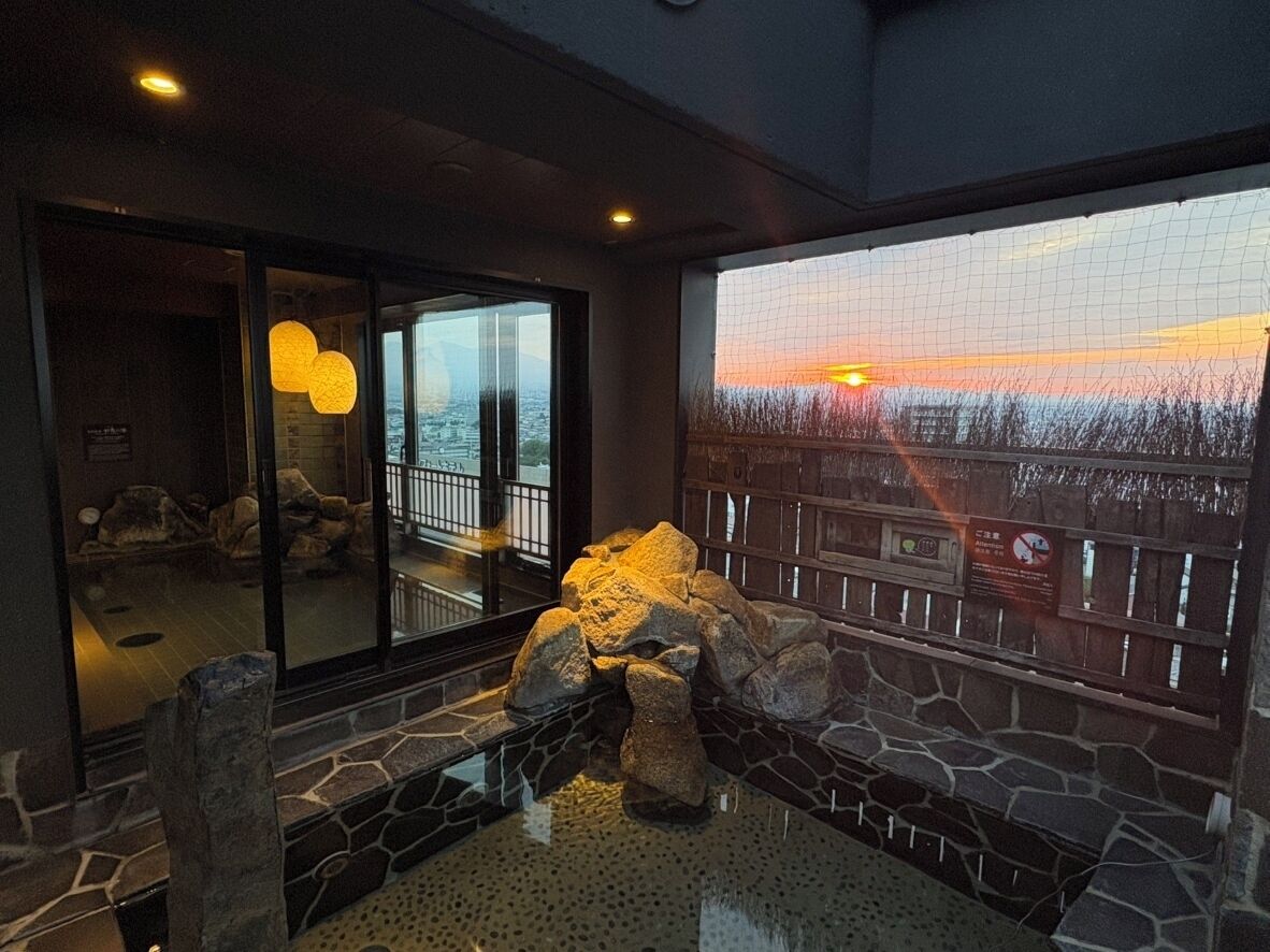 Una habitación con pared de piedra, ventana con vista a un atardecer y cerca de madera.