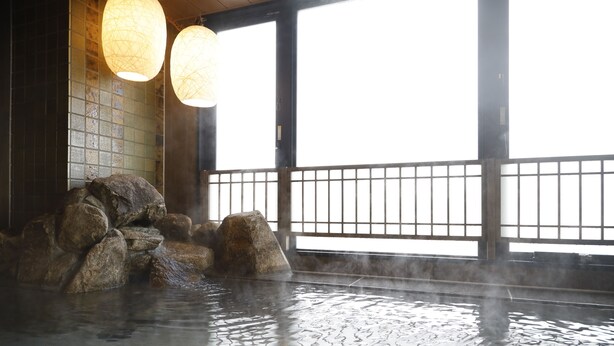Un onsen japonais traditionnel, avec un bain en pierre entouré de rochers, de grandes fenêtres et des lanternes en papier suspendues.