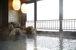 A traditional Japanese onsen with a stone bath surrounded by rocks, large windows, and hanging paper lanterns. - Dormy Inn Maebashi Natural Hot Spring (Maebashi)