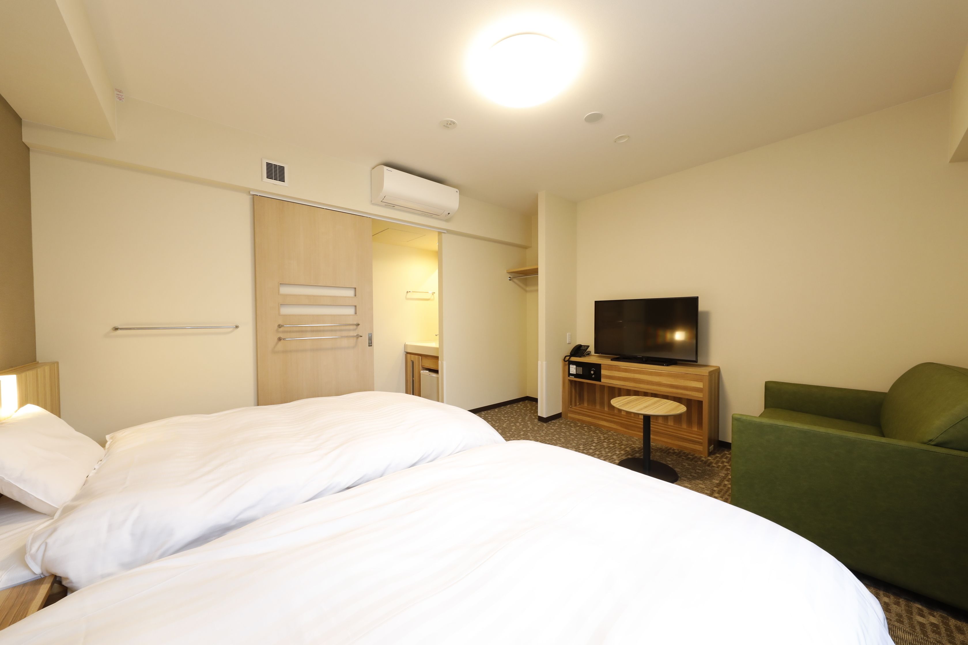 Une chambre d’hôtel avec un grand lit, une télévision, un fauteuil vert et une petite table.