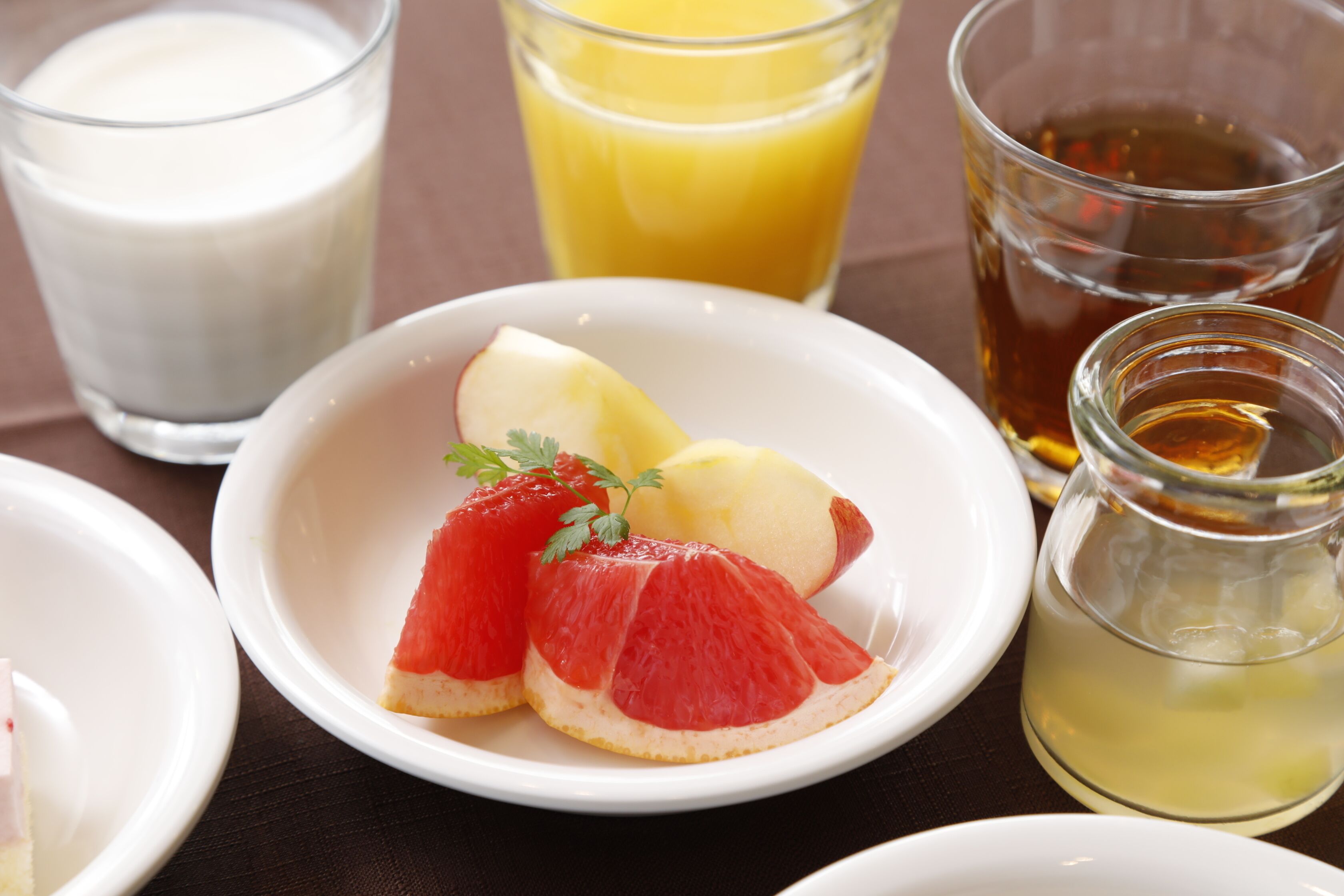 Desayuno con un plato de pomelo y rodajas de manzana, un vaso de jugo de naranja, un vaso de leche y una taza de té.