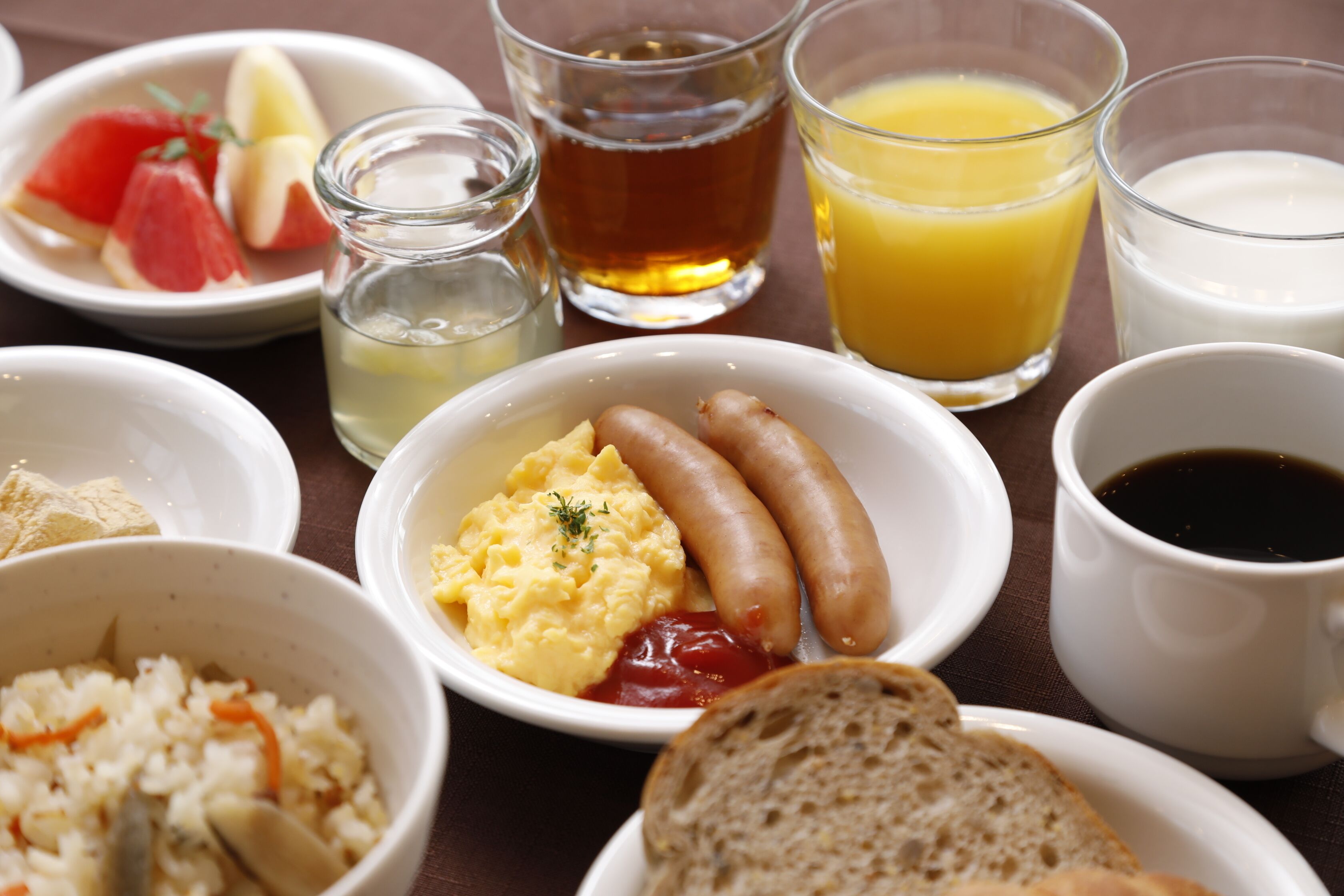 A breakfast setting with various dishes including sausages, scrambled eggs, toast, and beverages.