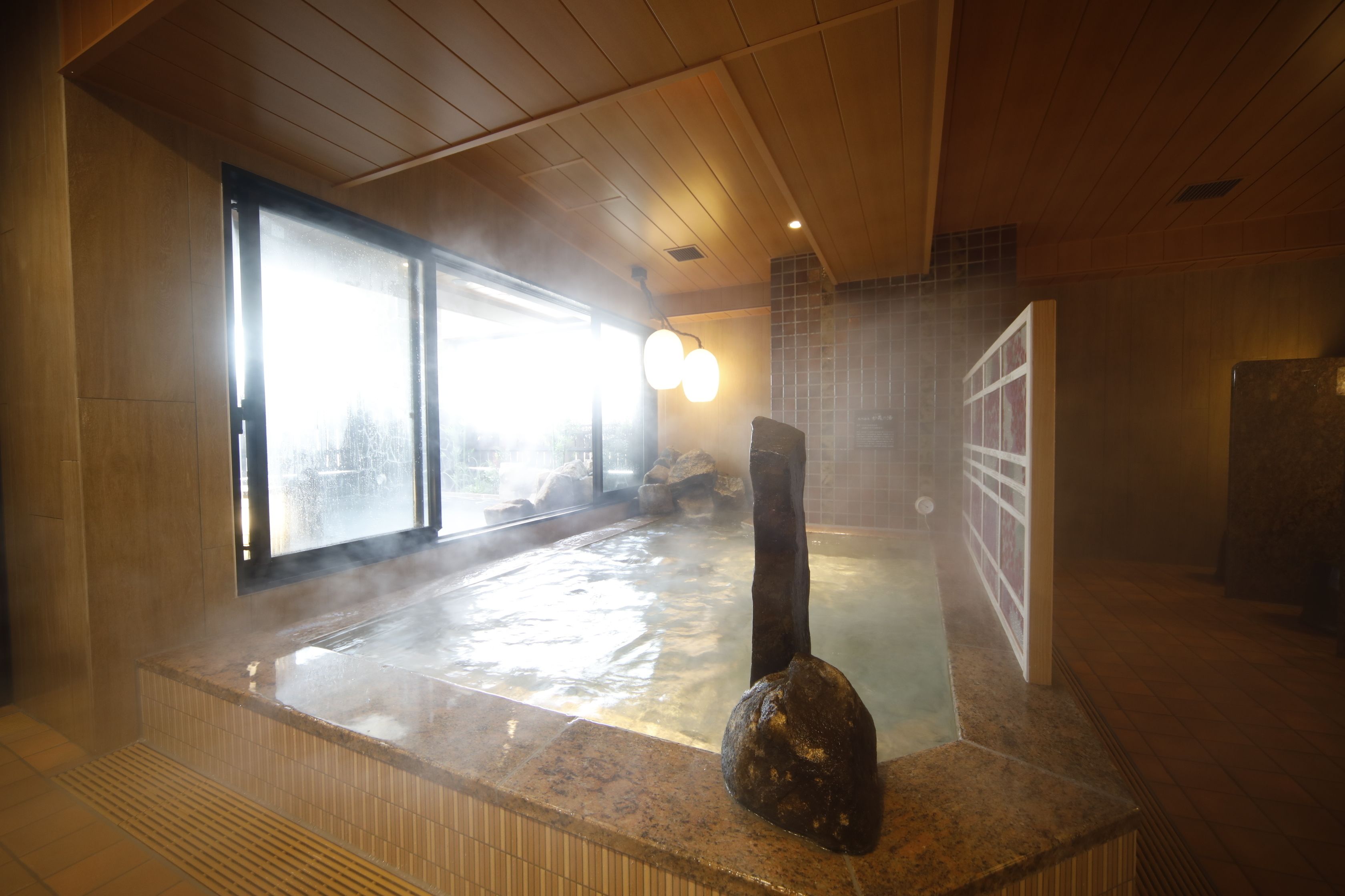 Un área de baños termales con una escultura de piedra, techo de madera y paredes de azulejos.