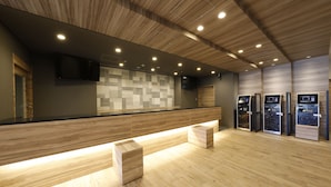 Un espace d’accueil moderne doté d’un plancher en bois, d’un comptoir avec un téléviseur et de trois bornes en libre-service.