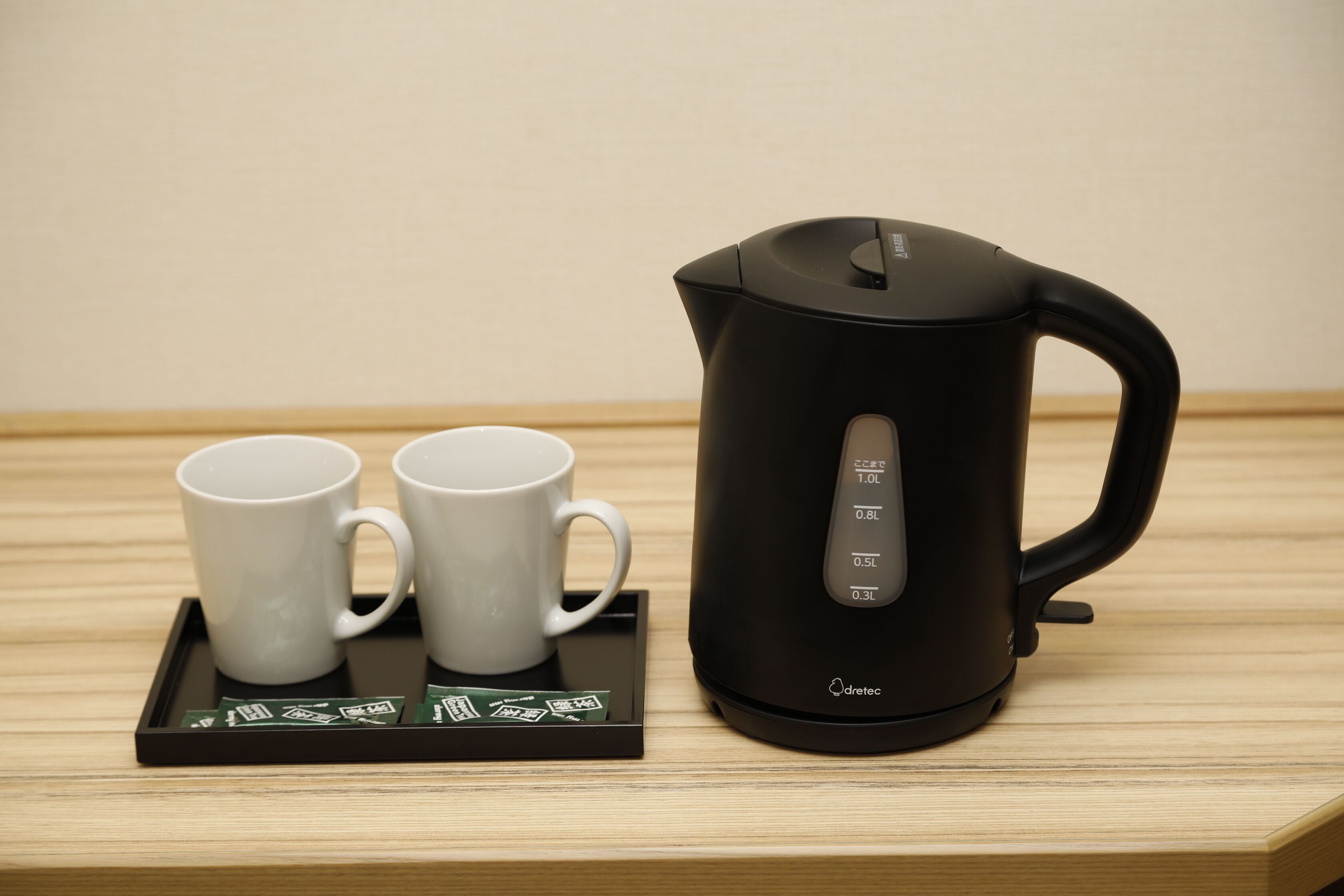 A black electric kettle with measurement markings and two white mugs on a tray.