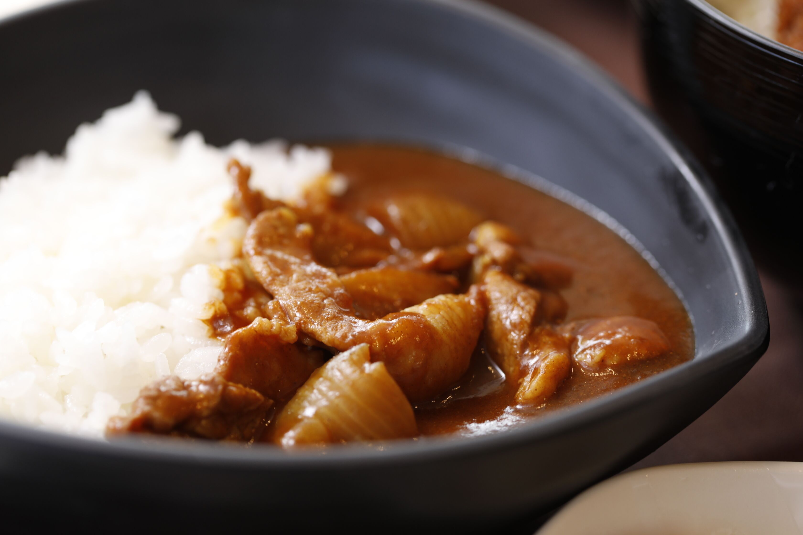 Uma tigela de arroz branco e um prato de curry com pedaços de carne e cebola.