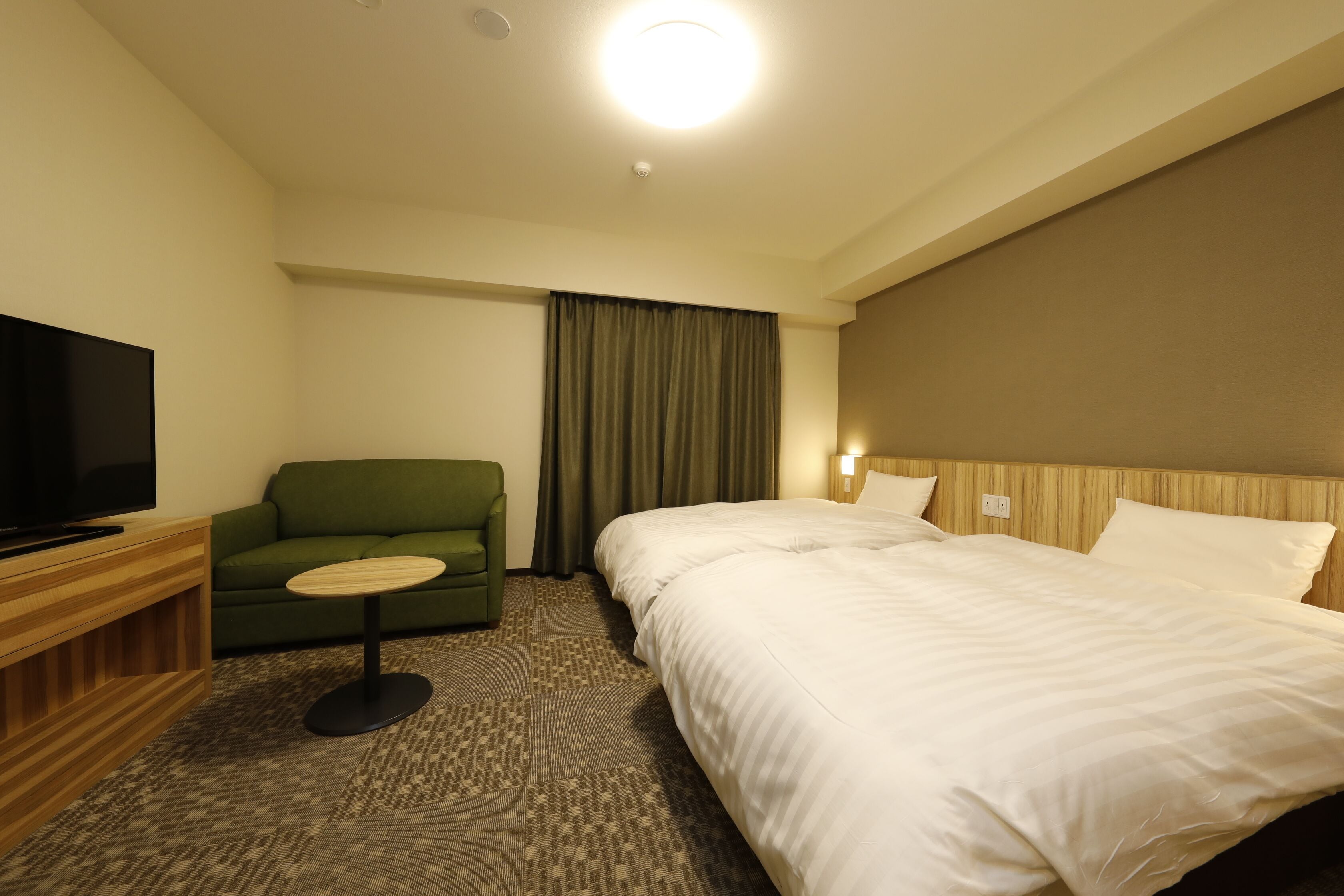 A hotel room with a bed, a television, a green armchair, and a small table.