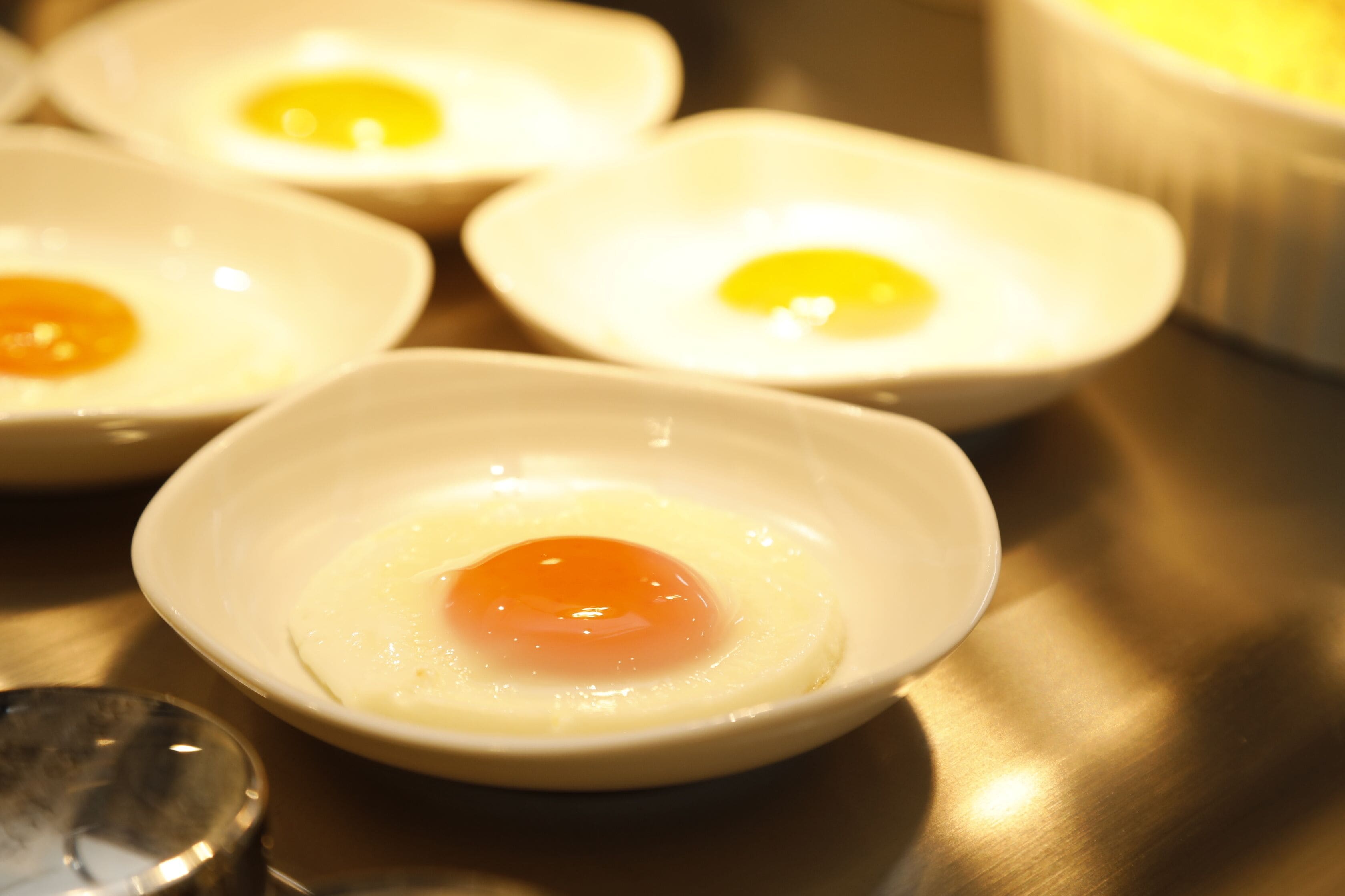 Four small white bowls containing fried eggs.