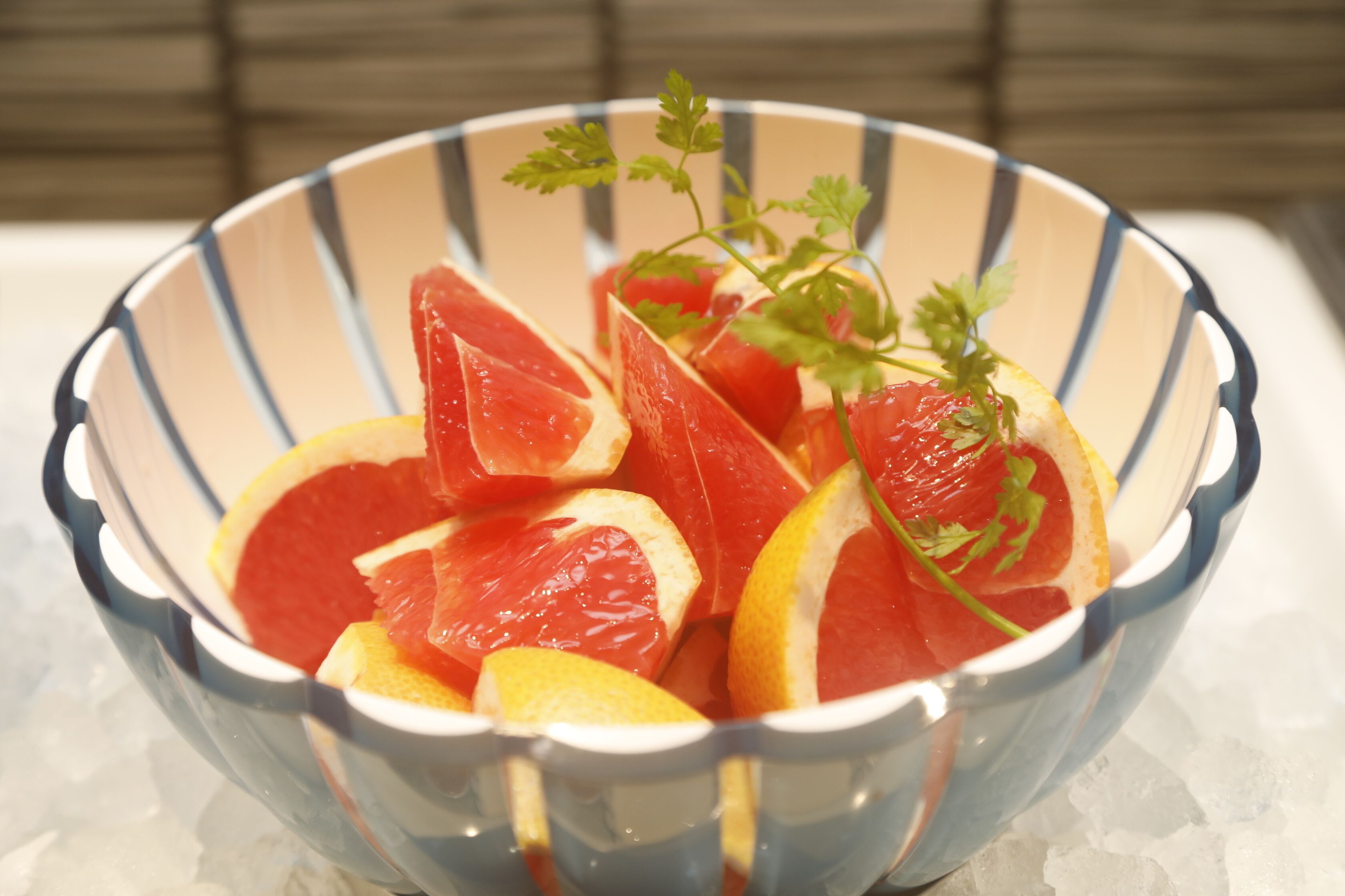 A bowl of sliced grapefruit and oranges with a sprig of parsley on a white surface.