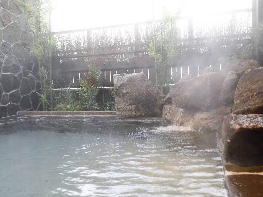A hot spring area with a stone wall, wooden fence, and rocks.