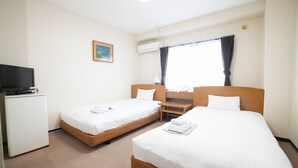 A hotel room with two single beds, a desk, a television, and an air conditioning unit.
