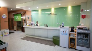A hotel reception area with a green wall, a reception desk, a clock, and a vending machine.