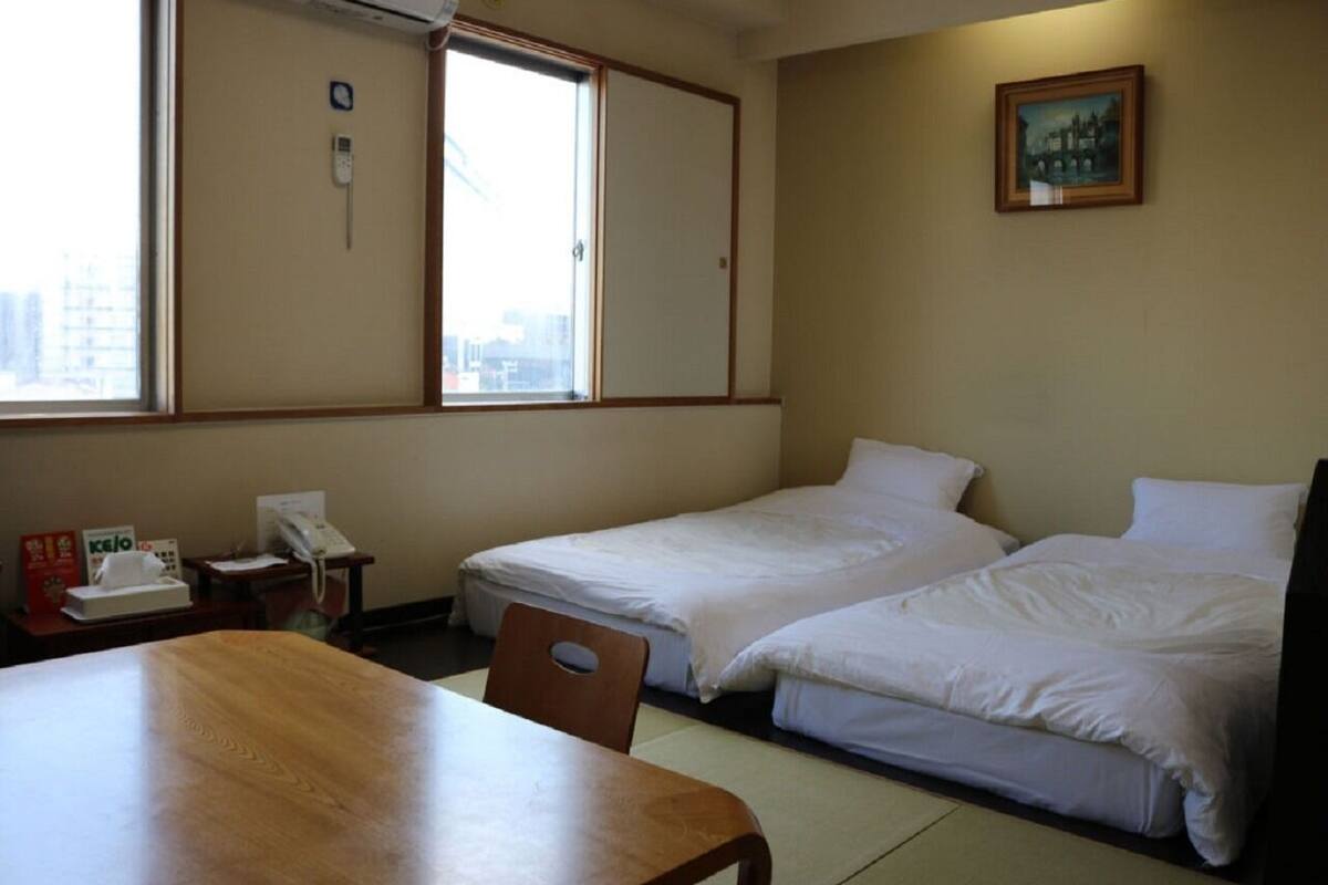 Hotellihuone, jossa on kaksi erillistä sänkyä, puinen pöytä, tuoli, kirjoituspöytä puhelimella sekä ikkuna, josta on näkymä rakennuksiin.