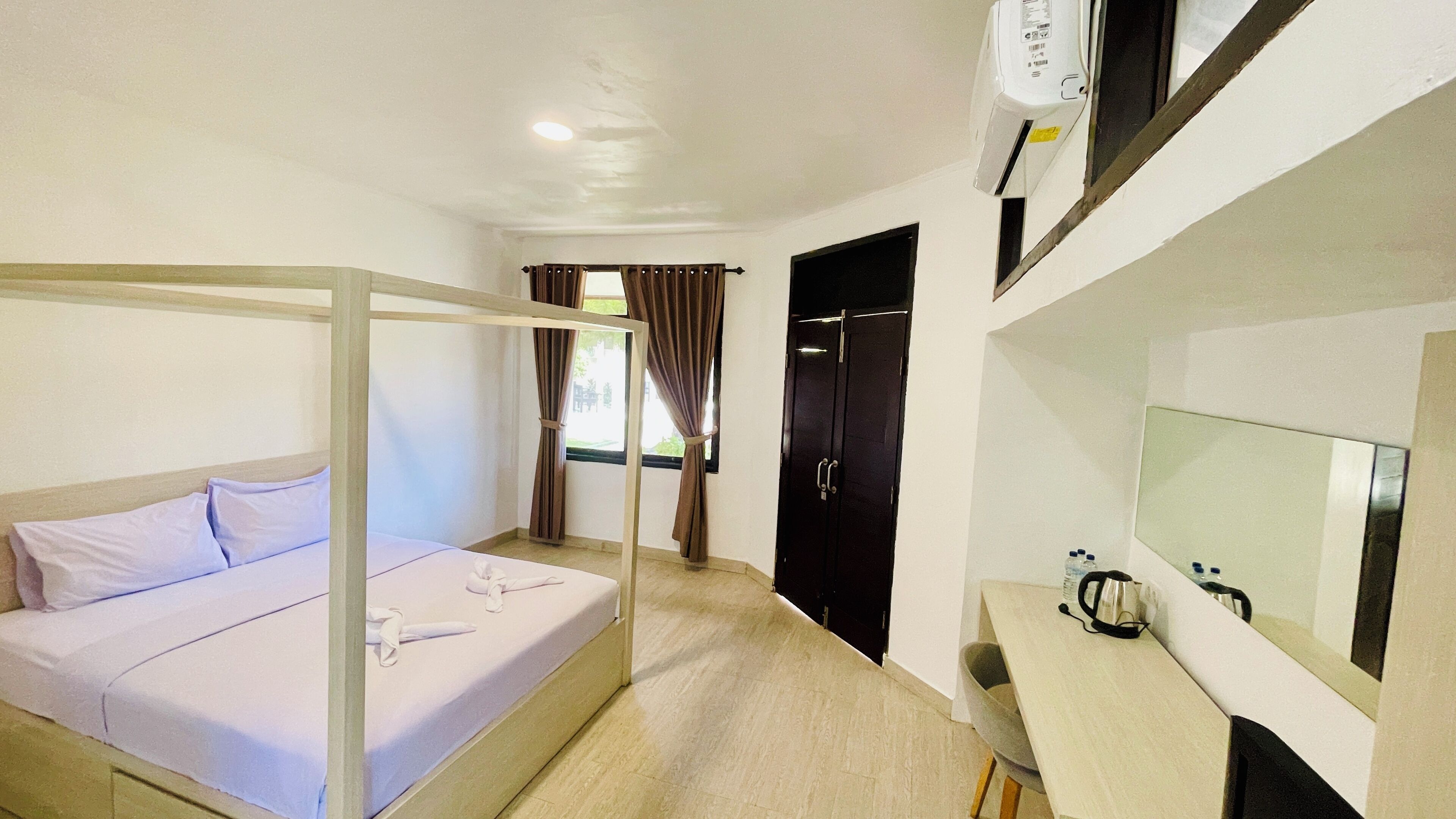 A hotel room with a single bed, a desk with a mirror, a wardrobe, and a window with curtains.
