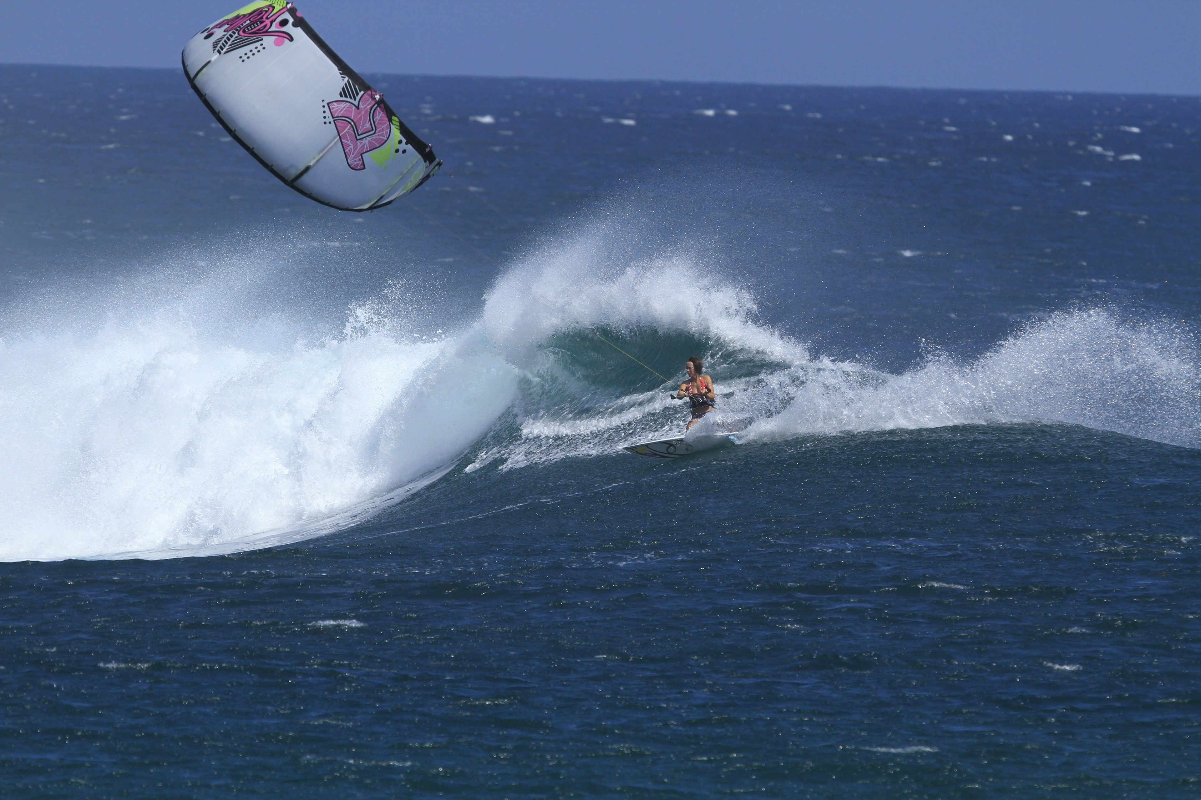 A person kite surfing on a wave with a colorful kite in the air.