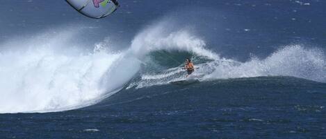 A person kite surfing on a wave with a colorful kite in the air.