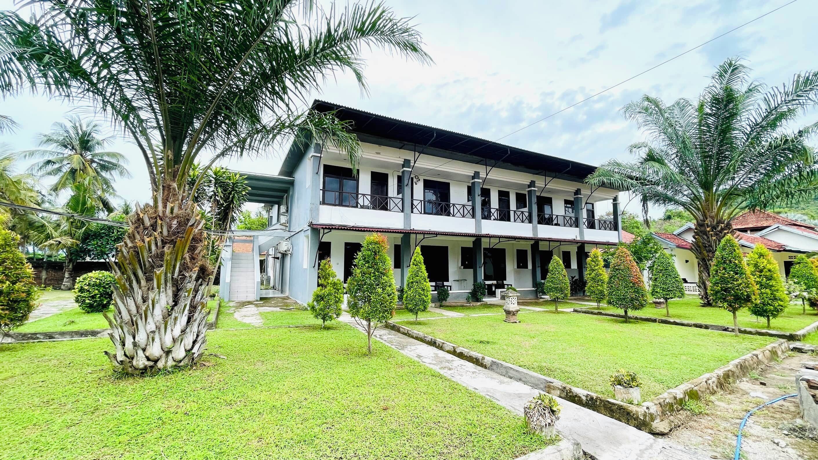 A two-story building with a covered balcony, surrounded by well-maintained lawns and palm trees.