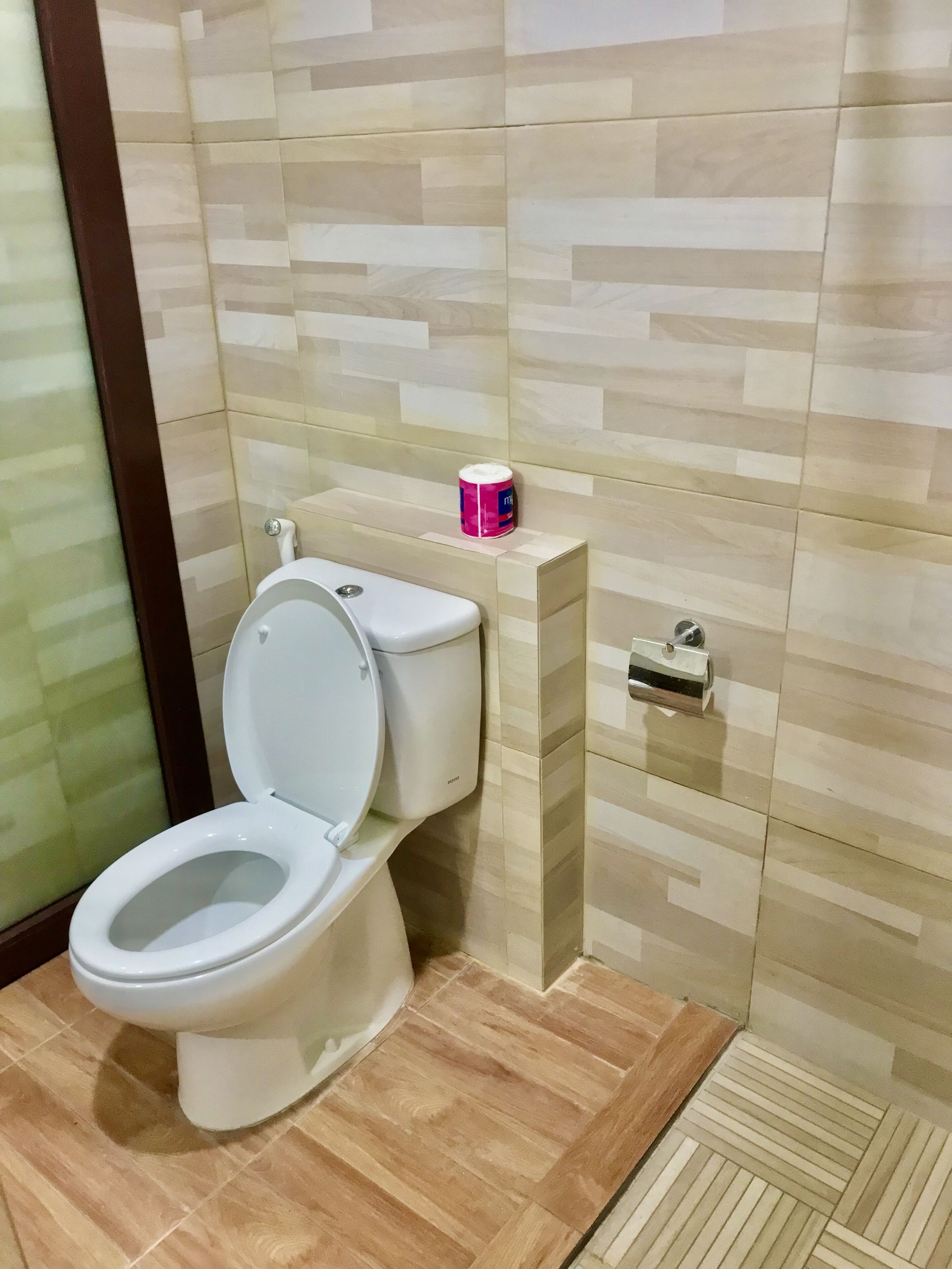 Et badeværelse med toilet, bidet og en lille hylde med en beholder.
