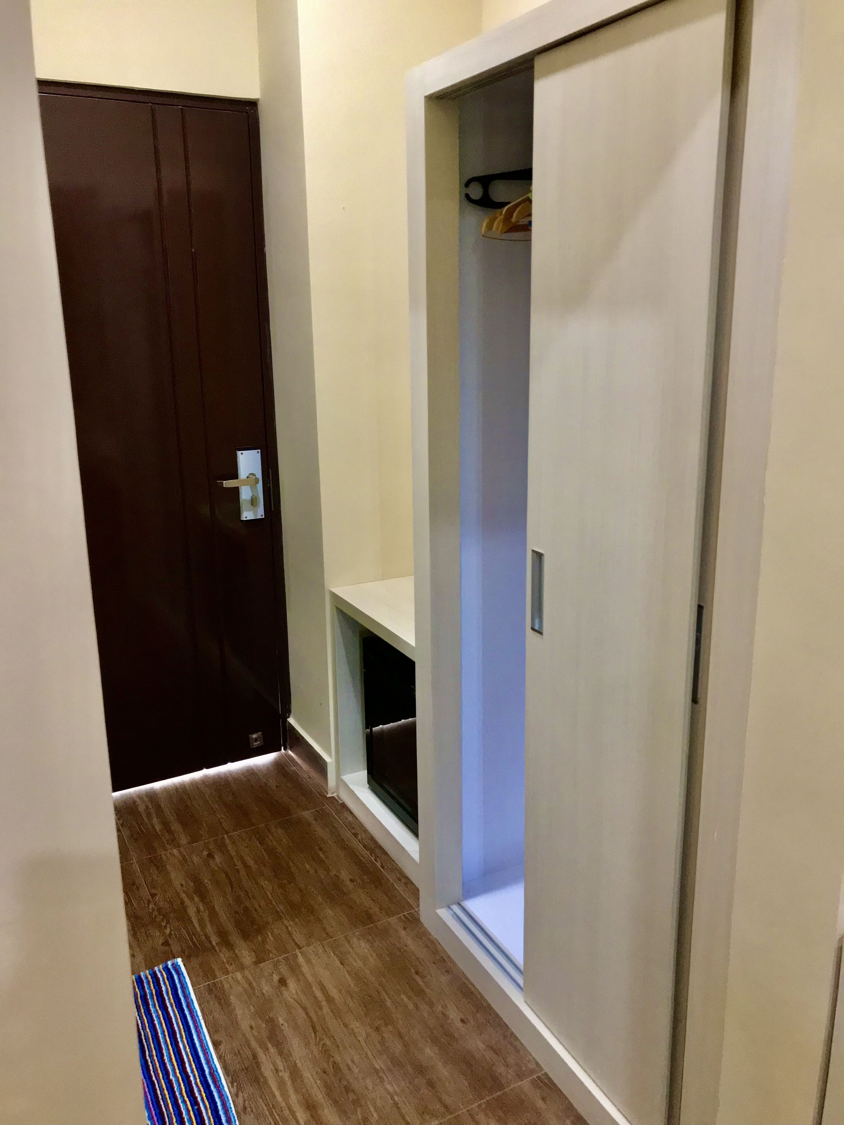 Un couloir avec une porte marron, une armoire blanche avec une étagère et un tapis bleu à rayures.