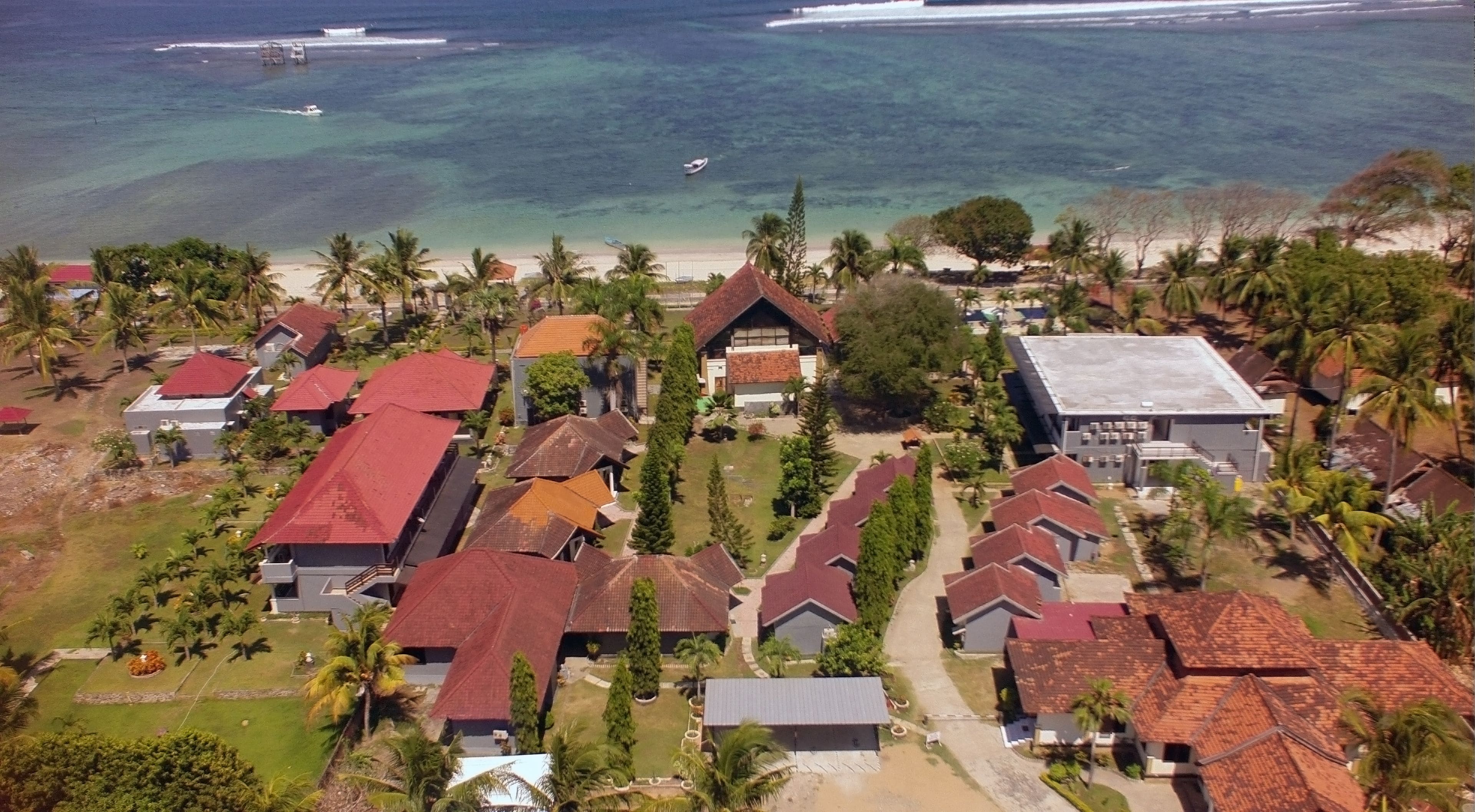 Luchtbeeld van een kustgebied met woonhuizen, palmbomen en een strand.