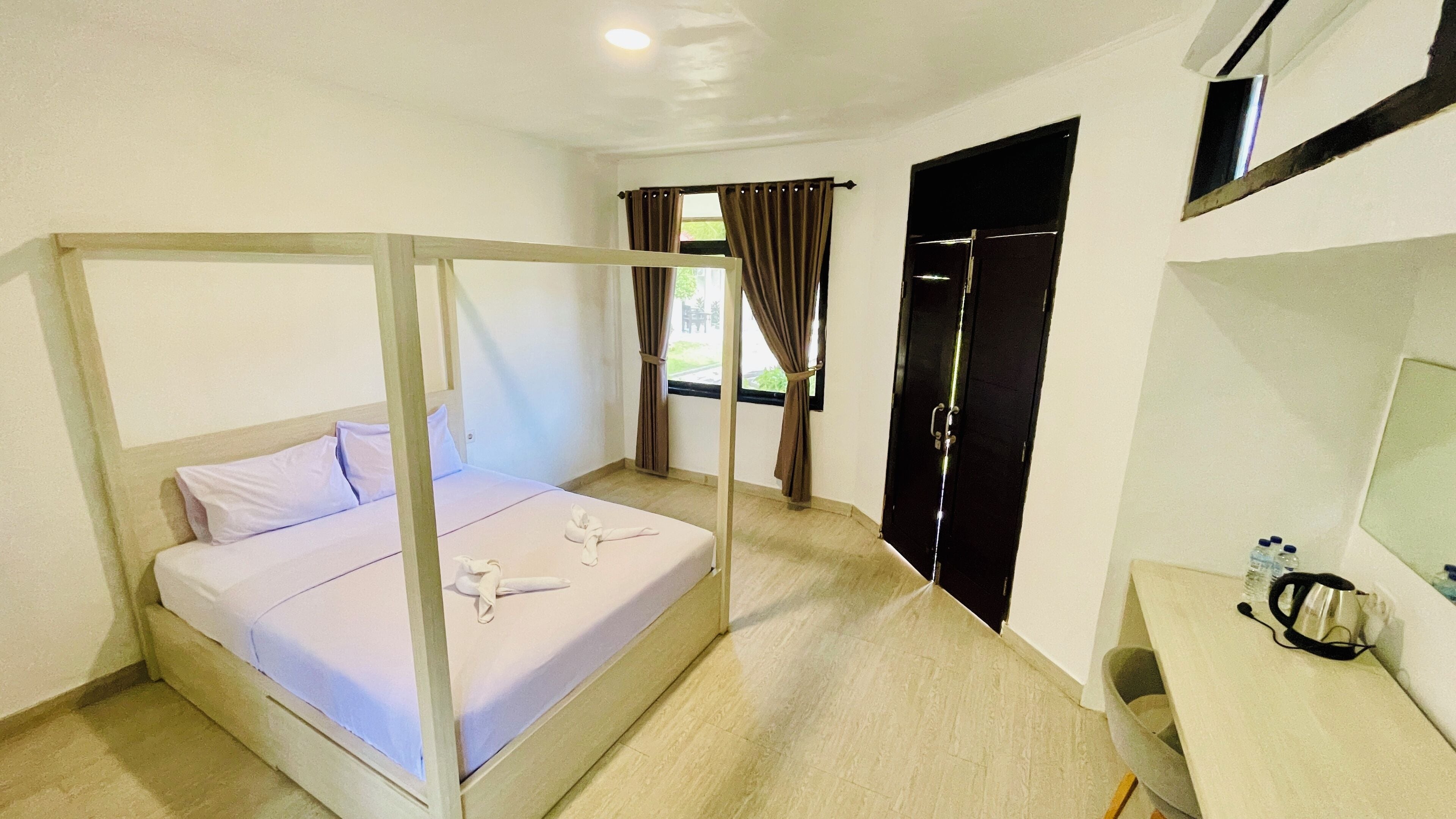 A hotel room with a four-poster bed, a desk with a kettle, and a wardrobe.