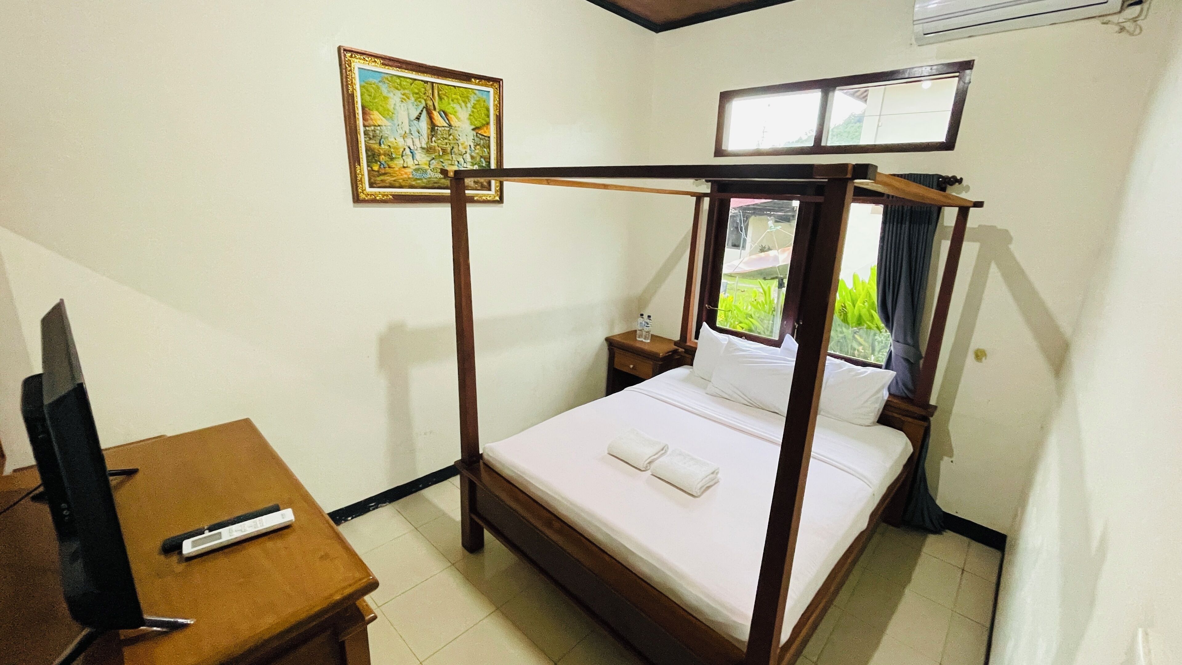 Una habitación con una cama con dosel, una mesita de noche con un control remoto, un cuadro en la pared y una ventana con cortinas.