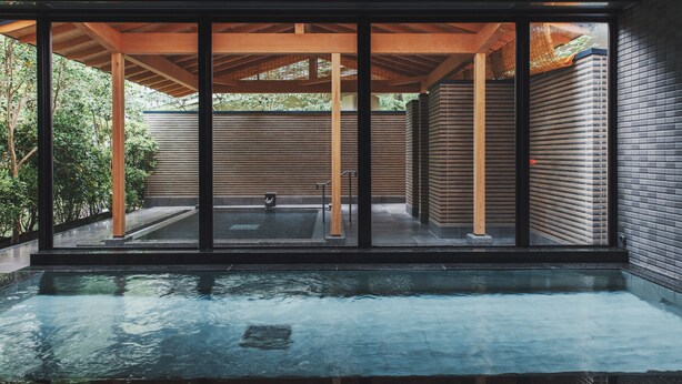 A modern indoor pool area with a wooden pergola, large windows, and a view of the surrounding greenery. - The Key Highland Nasu (Nasu)