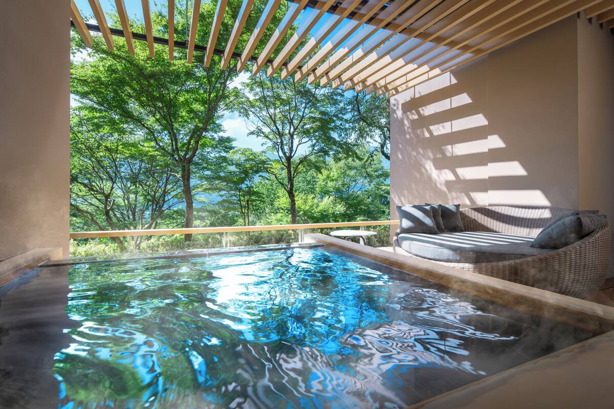 Un bain à remous avec vue sur les arbres, un canapé en osier et une pergola.