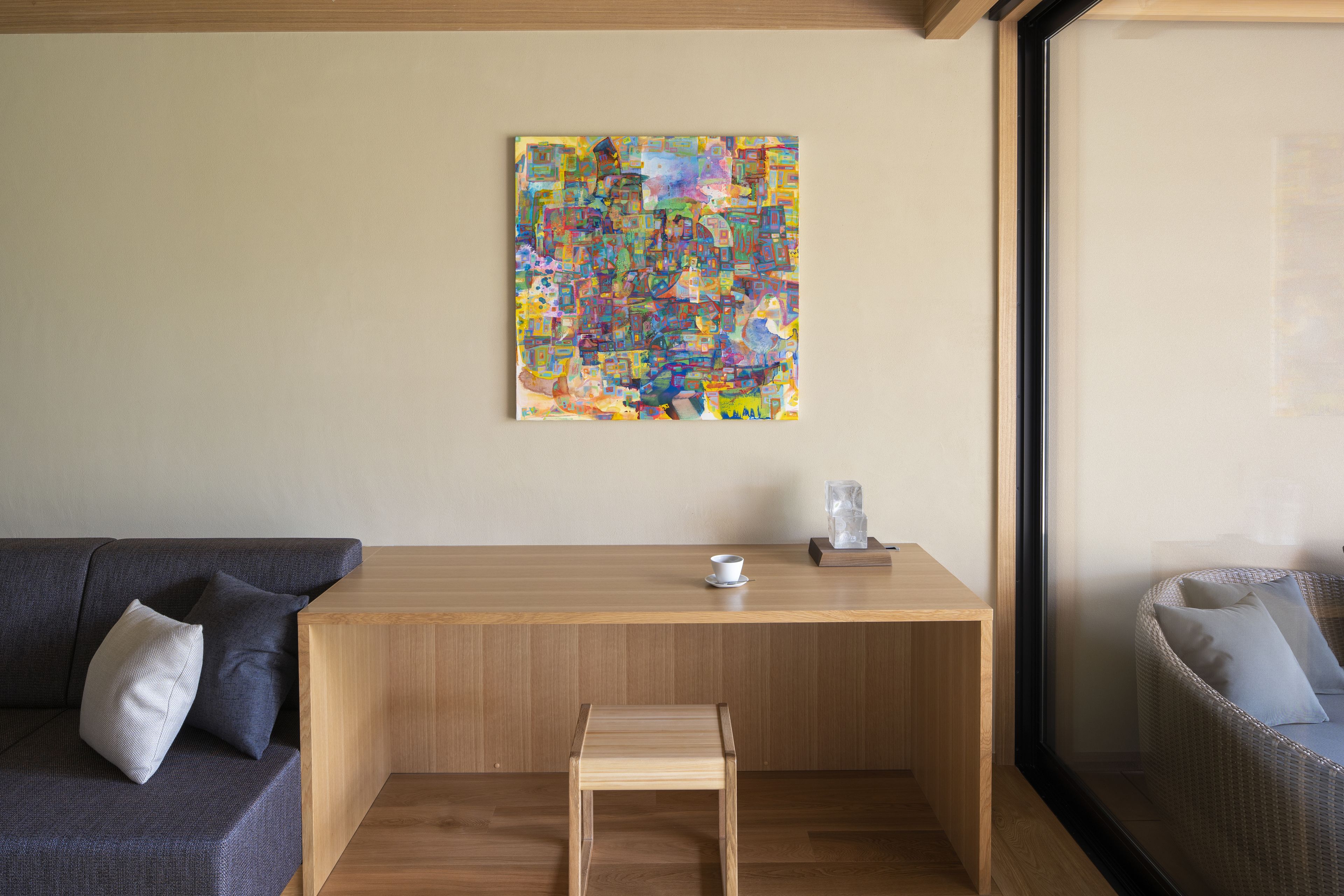 Un saló modern amb una taula baixa de fusta, un petit tamboret, un sofà amb coixins i un quadre abstracte i colorit a la paret.