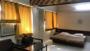 A hotel room with a bed, a desk, a chair, and curtains. - Maurya Residency (Pune)