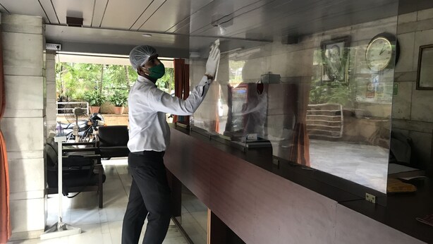 A person cleaning a glass partition in a room with a clock and a green sign on the wall. - Maurya Residency (Pune)