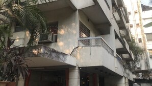 A multi-story building with balconies, a fan in the entrance, and a pile of leaves outside. - Maurya Residency (Pune)