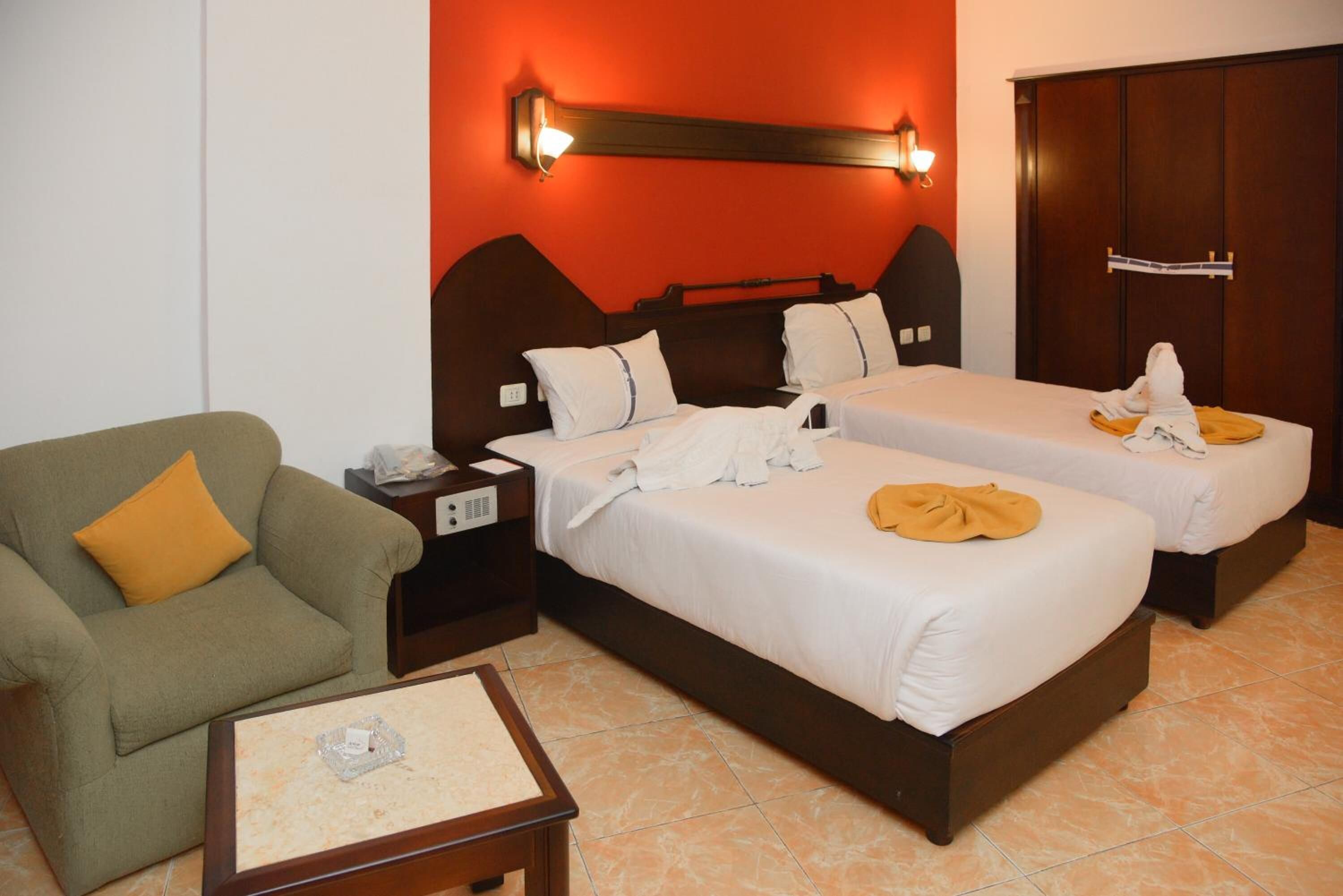 A hotel room with two beds, a chair, a nightstand, and a wardrobe.