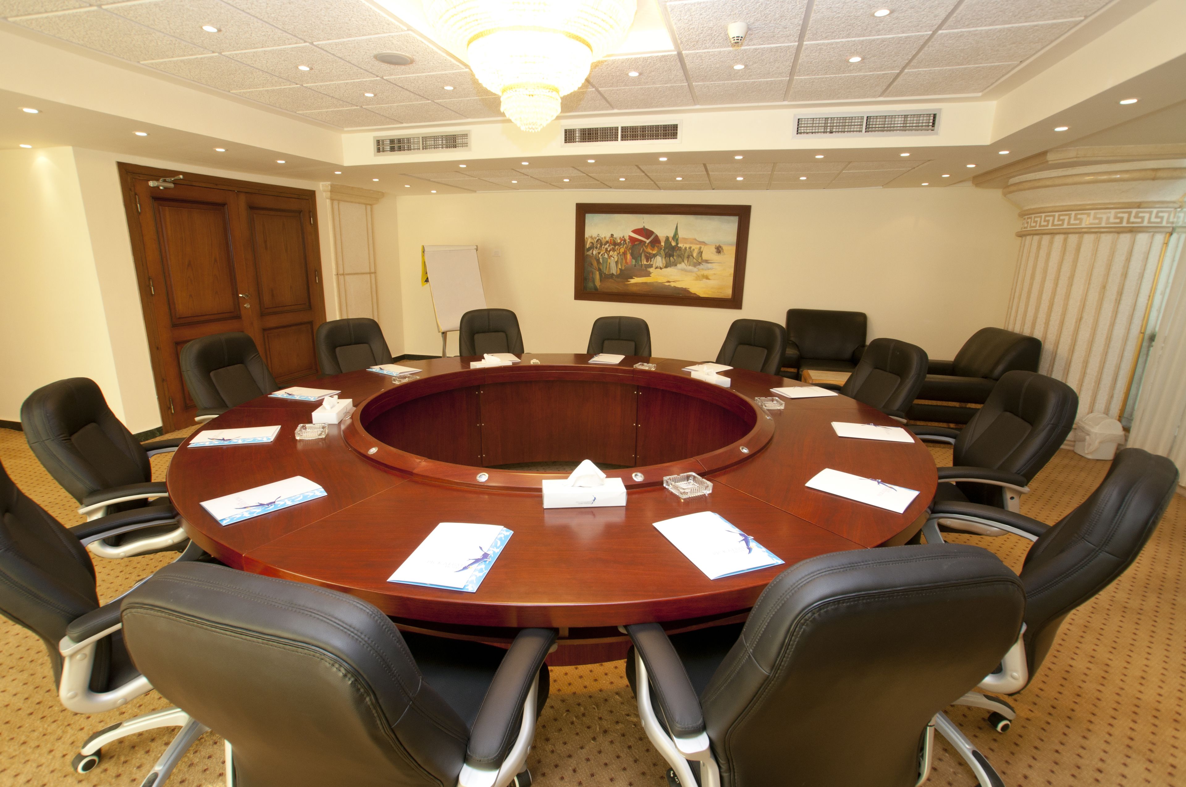 A conference room with a round table, black leather chairs, a whiteboard, and a painting on the wall.
