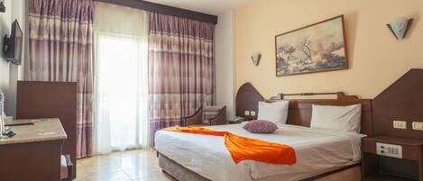 Habitación de hotel con una cama grande, un escritorio, una silla, una mesita de noche, un cuadro en la pared y una ventana con cortinas.